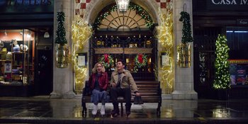 Movie still from “Last Christmas” (2019), directed by Paul Feig – A man and a woman sitting on a bench in front of christmas lights; Wide shot, Low angle