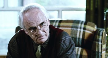 Movie still from “Last Night” (1998), directed by Don McKellar – An older man wearing glasses sitting on top of a couch; Close Up shot, Low angle