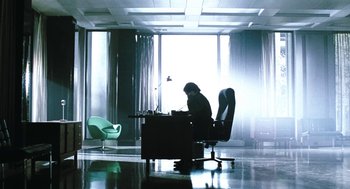 Movie still from “Last Night” (1998), directed by Don McKellar – A man sitting at a desk in a room; Wide shot, Low angle