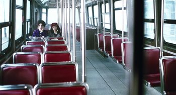 Movie still from “Last Night” (1998), directed by Don McKellar – Two people are sitting on a bus with red seats; Wide shot, High angle
