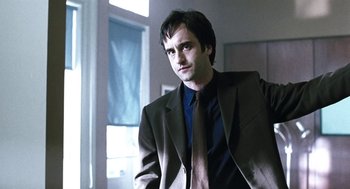 Movie still from “Last Night” (1998), directed by Don McKellar – A man wearing a suit and tie standing in a room; Close Up shot, Low angle