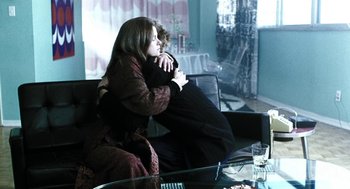 Movie still from “Last Night” (1998), directed by Don McKellar – A woman sitting on a man's lap in a living room; Medium shot, Over the shoulder angle