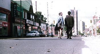 Movie still from “Last Night” (1998), directed by Don McKellar – Two people walking down the street on a sunny day; Wide shot, Low angle