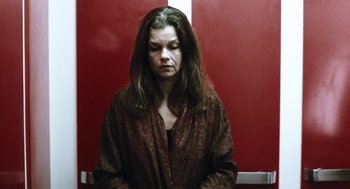 Movie still from “Last Night” (1998), directed by Don McKellar – A woman with long brown hair is standing in front of a red wall; Medium shot, Low angle