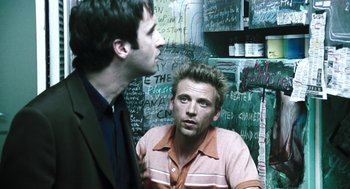 Movie still from “Last Night” (1998), directed by Don McKellar – Two men are talking in front of a wall of writing; Medium shot, Over the shoulder angle