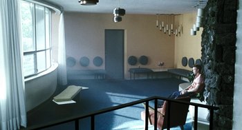 Movie still from “Last Night” (1998), directed by Don McKellar – A room that has a lot of speakers on the wall; Wide shot, High angle