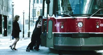 Movie still from “Last Night” (1998), directed by Don McKellar – Two people are kissing in front of a red bus; Wide shot, High angle