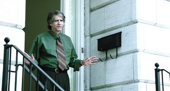 Movie still from “Last Night” (1998), directed by Don McKellar – A man in a green dress shirt and tie standing on a porch; Medium shot, Low angle