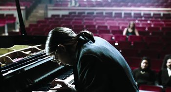 Movie still from “Last Night” (1998), directed by Don McKellar – A woman playing the piano in a large auditorium; Medium shot, High angle