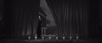 Movie still from “Last Year at Marienbad” (1961), directed by Alain Resnais – A black and white photo of a stage with curtains open; Extreme Wide shot, High angle