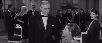Movie still from “Last Year at Marienbad” (1961), directed by Alain Resnais – An older man in a tuxedo talking to a woman in a gown; Medium shot, Over the shoulder angle