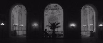 Movie still from “Last Year at Marienbad” (1961), directed by Alain Resnais – A person sitting on a chair in front of a window; Wide shot, Low angle