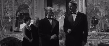 Movie still from “Last Year at Marienbad” (1961), directed by Alain Resnais – Two men and a woman in tuxedos standing in front of a mirror; Medium shot, Low angle