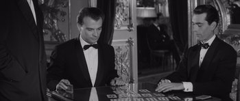 Movie still from “Last Year at Marienbad” (1961), directed by Alain Resnais – A man in a tuxedo playing a game of mahjongg; Medium shot, Over the shoulder angle