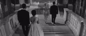 Movie still from “Last Year at Marienbad” (1961), directed by Alain Resnais – A group of people walking down a set of stairs; Wide shot, Low angle