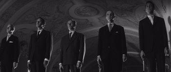 Movie still from “Last Year at Marienbad” (1961), directed by Alain Resnais – A group of men standing next to each other holding guns; Medium shot, Low angle