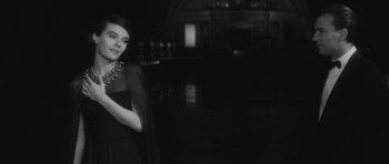 Movie still from “Last Year at Marienbad” (1961), directed by Alain Resnais – A black and white photo of a woman in a black dress; Medium shot, Over the shoulder angle