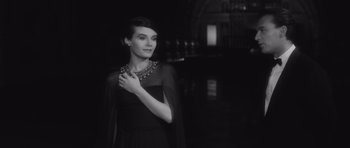 Movie still from “Last Year at Marienbad” (1961), directed by Alain Resnais – A black and white photo of a woman wearing a dress; Medium shot, Over the shoulder angle