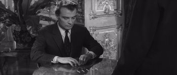 Movie still from “Last Year at Marienbad” (1961), directed by Alain Resnais – A black and white photo of a man sitting at a table; Medium shot, Over the shoulder angle
