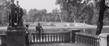 Movie still from “Last Year at Marienbad” (1961), directed by Alain Resnais – A black and white photo of a man sitting on a railing; Wide shot, High angle
