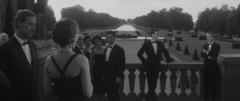 Movie still from “Last Year at Marienbad” (1961), directed by Alain Resnais – A black and white photo of a group of people in tuxedos; Wide shot, Over the shoulder angle