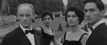 Movie still from “Last Year at Marienbad” (1961), directed by Alain Resnais – A black and white photo of three women and a man; Medium shot, Low angle