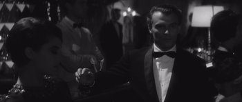 Movie still from “Last Year at Marienbad” (1961), directed by Alain Resnais – A black and white photo of a man holding a glass of wine; Close Up shot, Over the shoulder angle