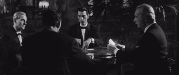 Movie still from “Last Year at Marienbad” (1961), directed by Alain Resnais – A man sitting at a table with two other men; Medium shot, High angle