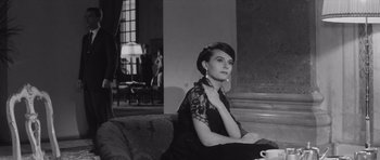 Movie still from “Last Year at Marienbad” (1961), directed by Alain Resnais – A woman sitting on top of a couch in a living room; Medium shot, Low angle