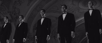 Movie still from “Last Year at Marienbad” (1961), directed by Alain Resnais – Two men in tuxedos stand next to each other; Medium shot, Low angle