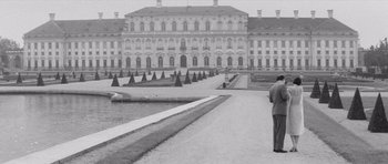 Movie still from “Last Year at Marienbad” (1961), directed by Alain Resnais – A man standing on a path in front of a large building; Wide shot, Low angle