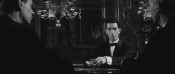 Movie still from “Last Year at Marienbad” (1961), directed by Alain Resnais – A black and white photo of a man sitting at a table; Medium shot, Over the shoulder angle
