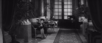 Movie still from “Last Year at Marienbad” (1961), directed by Alain Resnais – A woman sitting on top of a bench next to a window; Wide shot, High angle