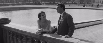 Movie still from “Last Year at Marienbad” (1961), directed by Alain Resnais – A man and a woman sitting next to each other on a ledge; Medium shot, Low angle