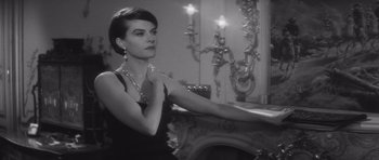 Movie still from “Last Year at Marienbad” (1961), directed by Alain Resnais – A black and white photo of a woman in a black dress; Medium shot, Over the shoulder angle