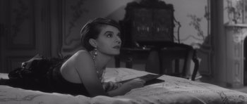 Movie still from “Last Year at Marienbad” (1961), directed by Alain Resnais – A woman laying on a bed holding a knife; Close Up shot, High angle