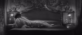 Movie still from “Last Year at Marienbad” (1961), directed by Alain Resnais – A black and white photo of a dog laying on a bed; Medium shot, High angle