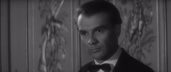 Movie still from “Last Year at Marienbad” (1961), directed by Alain Resnais – Black and white photograph of a man wearing a tuxedo; Close Up shot, Over the shoulder angle