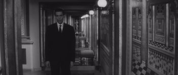 Movie still from “Last Year at Marienbad” (1961), directed by Alain Resnais – A man in a suit standing in a hallway; Medium shot, Low angle