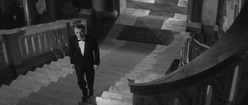 Movie still from “Last Year at Marienbad” (1961), directed by Alain Resnais – A man in a tuxedo walking down the stairs of a building; Wide shot, High angle