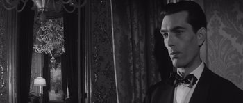 Movie still from “Last Year at Marienbad” (1961), directed by Alain Resnais – A black and white photo of a man in front of a curtain; Close Up shot, Low angle