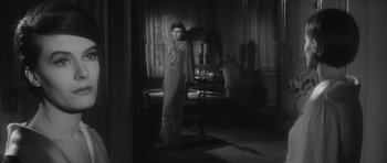 Movie still from “Last Year at Marienbad” (1961), directed by Alain Resnais – A black and white photo of a woman standing in front of a mirror; Wide shot, High angle