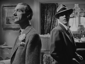 Movie still from “Laura” (1944), directed by Rouben Mamoulian – A man in a suit standing next to another man in a hat; Medium shot, Low angle