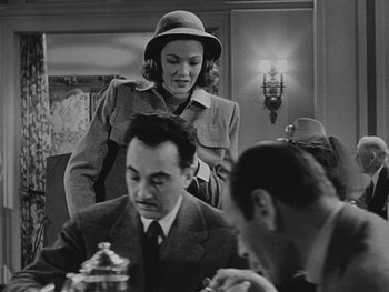 Movie still from “Laura” (1944), directed by Rouben Mamoulian – A woman standing next to a man at a dinner table; Medium shot, Over the shoulder angle
