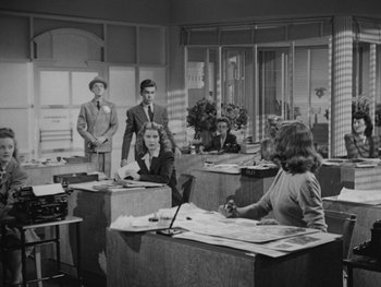 Movie still from “Laura” (1944), directed by Rouben Mamoulian – A group of men and a woman sitting at a desk; Wide shot, High angle