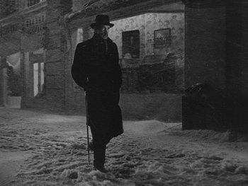 Movie still from “Laura” (1944), directed by Rouben Mamoulian – A black and white photo of a man in a long coat and hat; Wide shot, Low angle