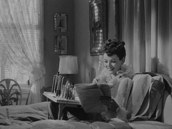 Movie still from “Laura” (1944), directed by Rouben Mamoulian – A woman sitting on a bed reading a magazine; Medium shot, High angle