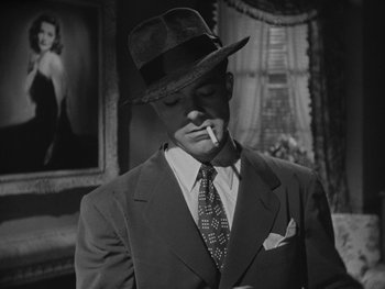 Movie still from “Laura” (1944), directed by Rouben Mamoulian – A black and white photo of a man smoking a cigarette; Close Up shot, Low angle