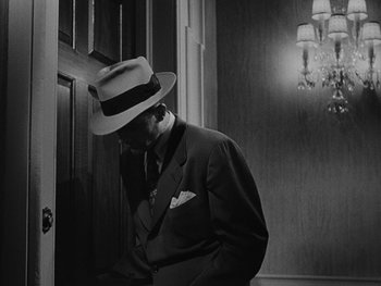 Movie still from “Laura” (1944), directed by Rouben Mamoulian – A black and white photo of a man in a suit and hat; Medium shot, Low angle