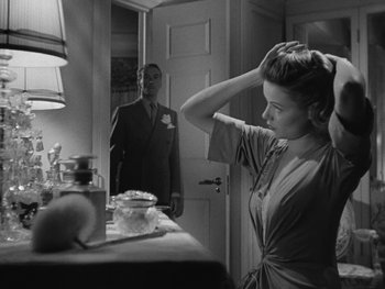 Movie still from “Laura” (1944), directed by Rouben Mamoulian – A woman standing in front of a mirror with a man standing in the background; Medium shot, Over the shoulder angle